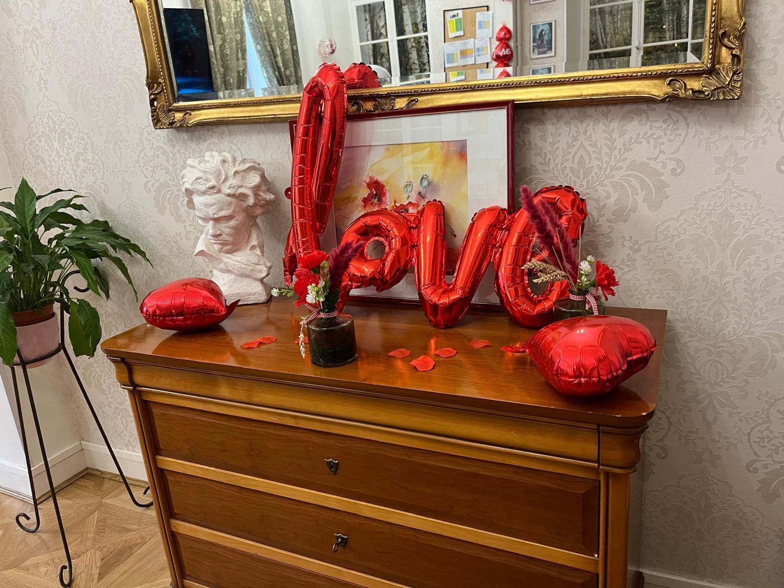 Commode en bois décorée de ballons rouges en forme de cœur et d'un ballon rouge « love » sous un miroir à cadre doré