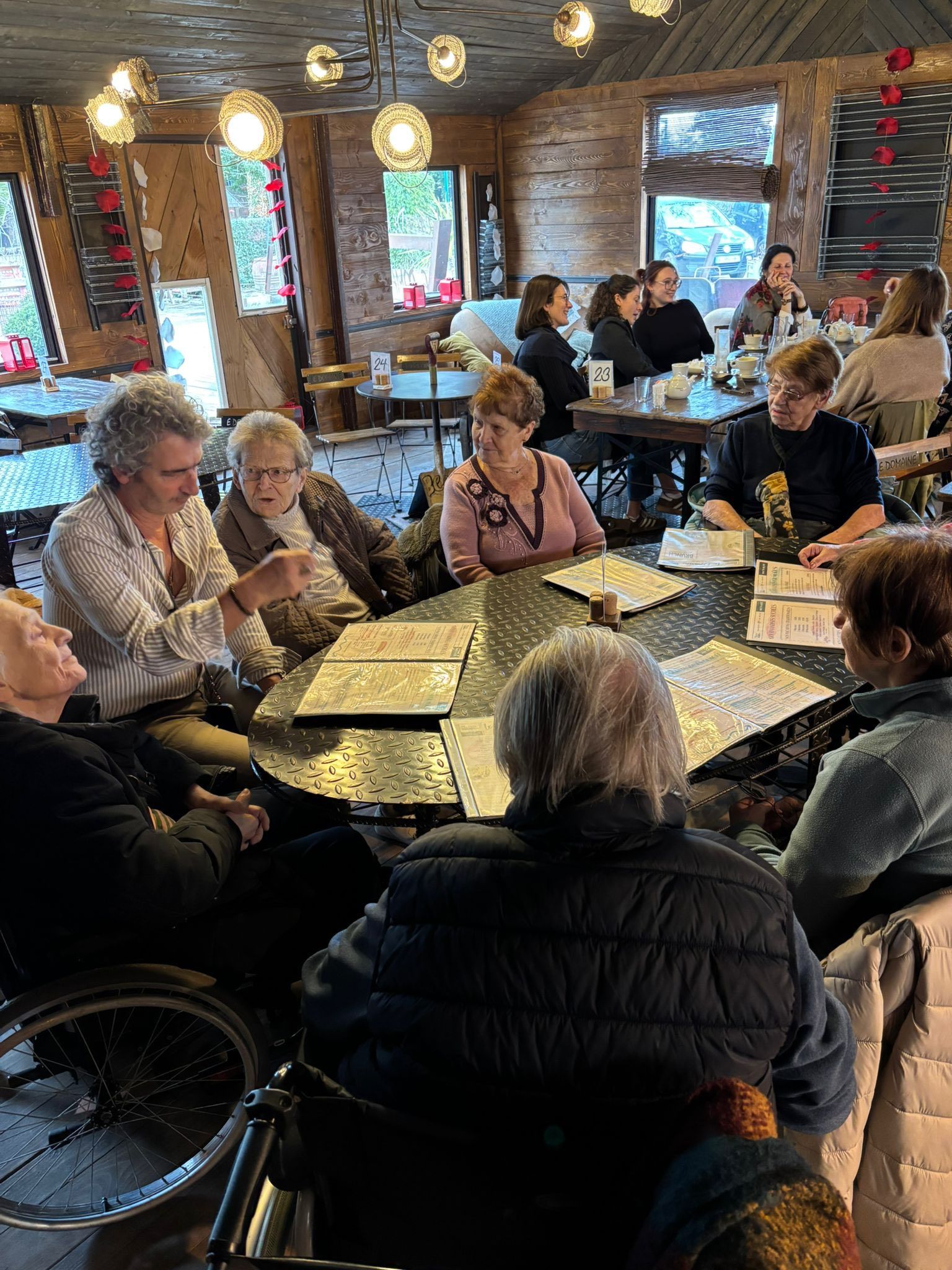 Des gens assis autour de tables dans un café ou un pub chaleureux, éclairé par une lumière douce et orné de vitraux.