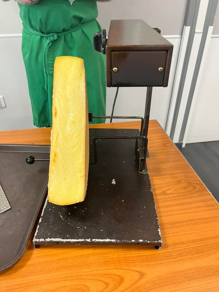 Un morceau de fromage jaune sur un présentoir noir, à côté d'une petite armoire sombre posée sur une table en bois.