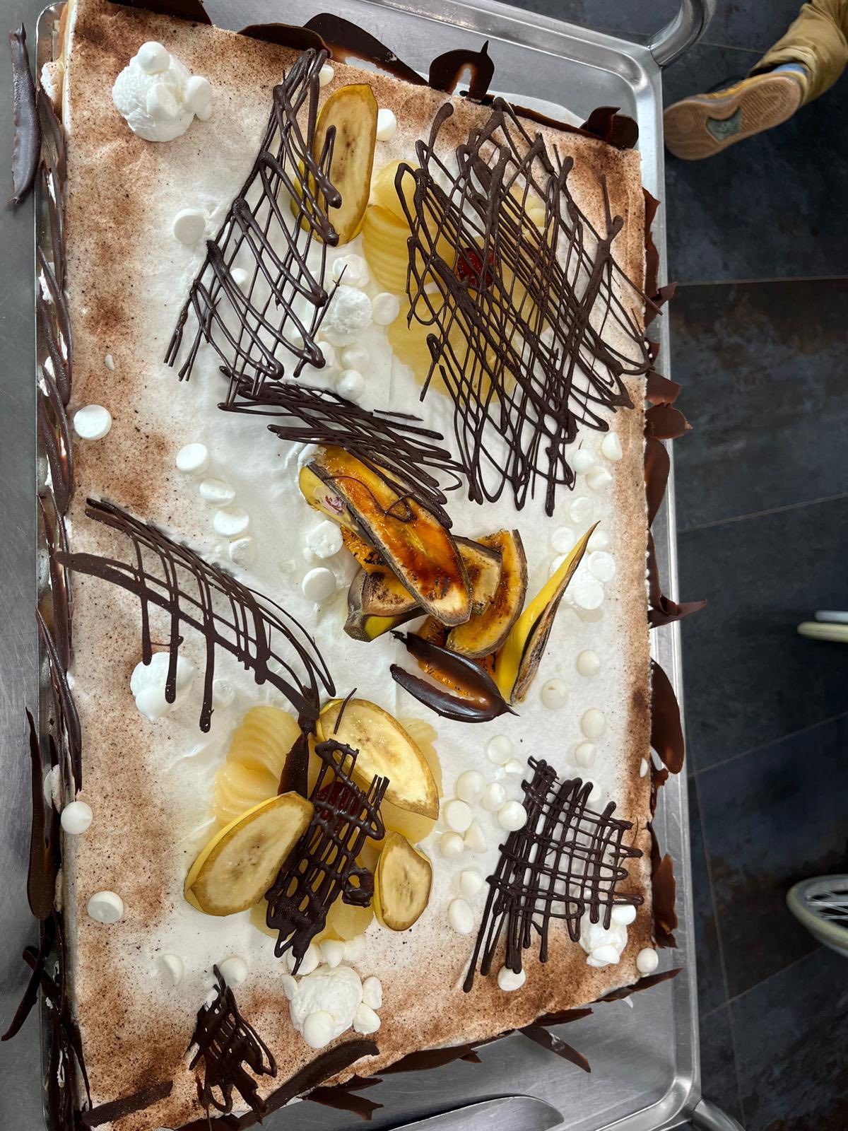 Gâteau rectangulaire décoré de glaçage blanc, d'un filet de chocolat et de tranches d'orange, présenté sur un plateau.