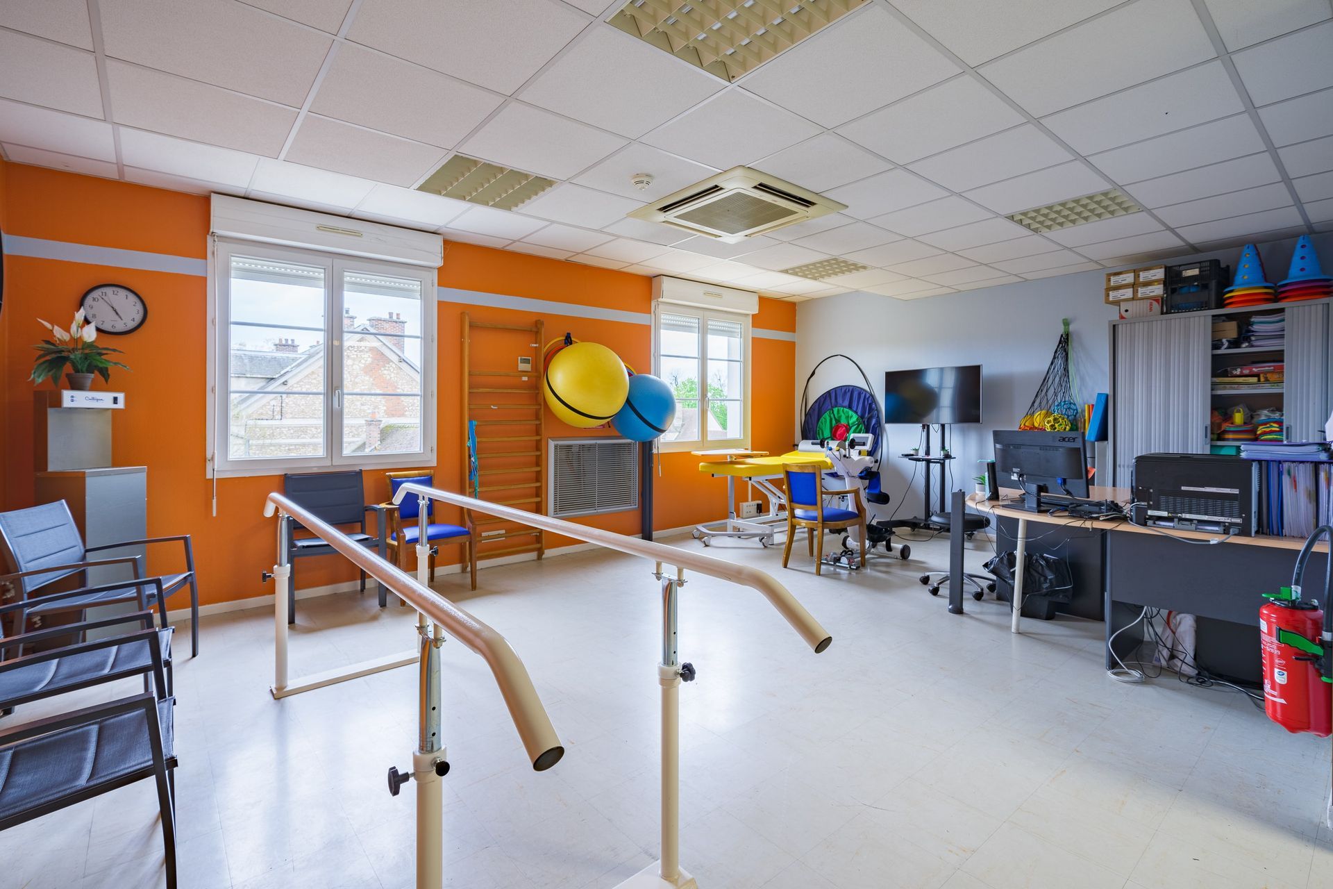 Salle de physiothérapie avec barres parallèles, appareils d'exercice, miroirs et murs colorés