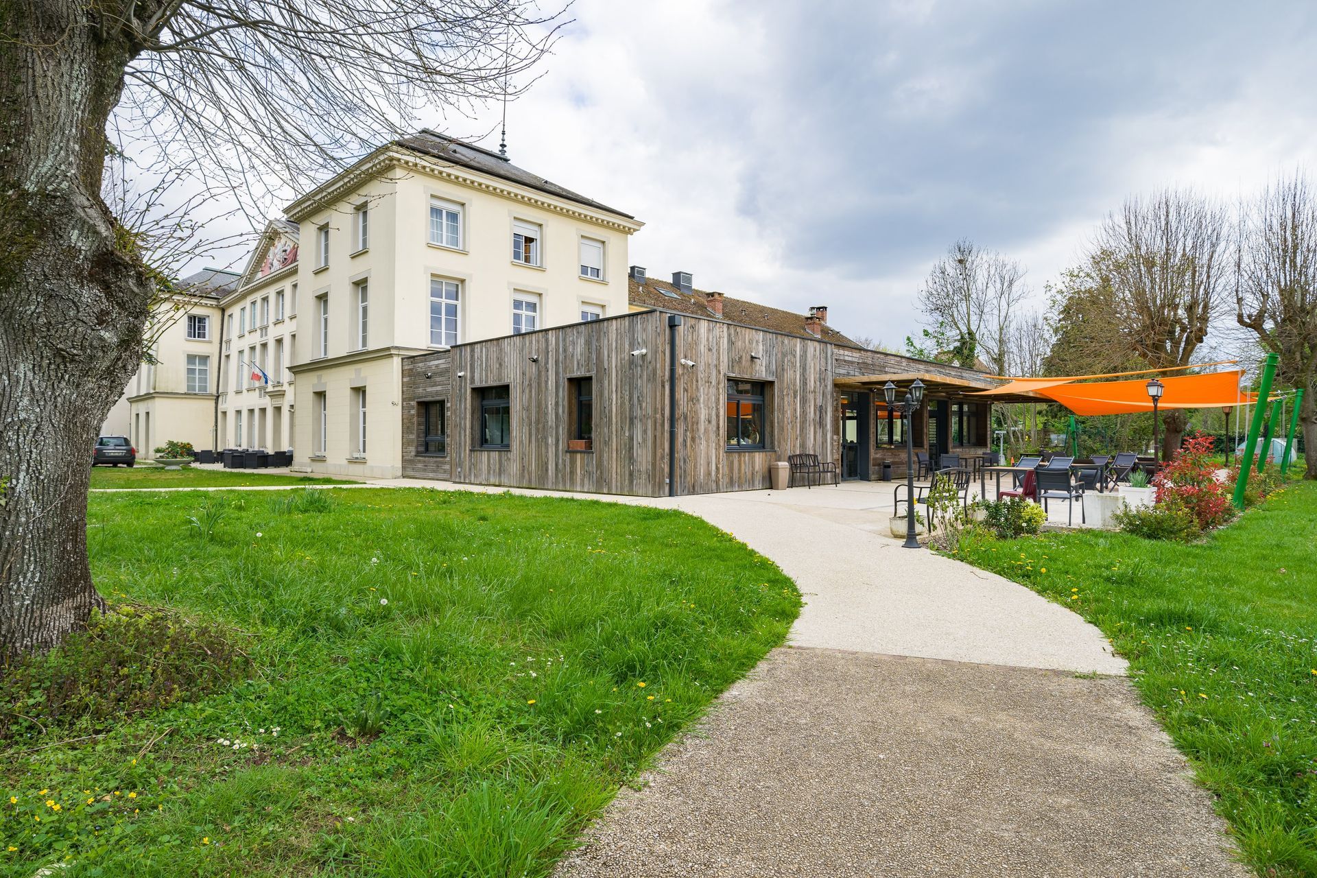 Bâtiment moderne avec terrasse donnant sur un chemin sinueux et une pelouse verdoyante.