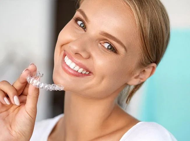 Una mujer sonríe mientras sostiene un aparato transparente en sus dientes.
