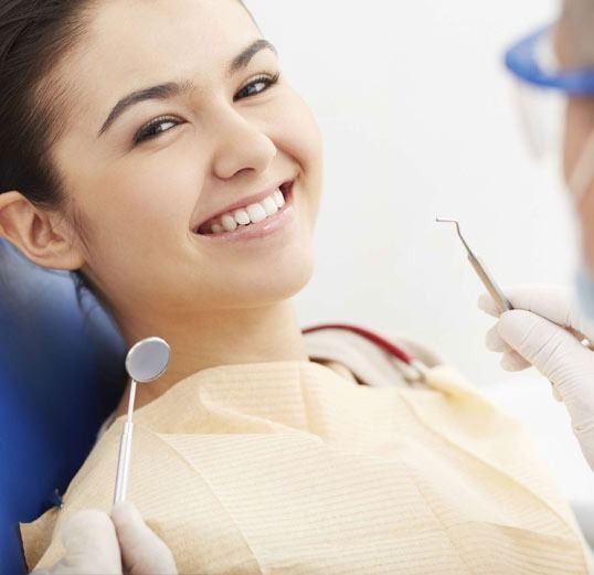 Una mujer sonríe mientras un dentista le examina los dientes.