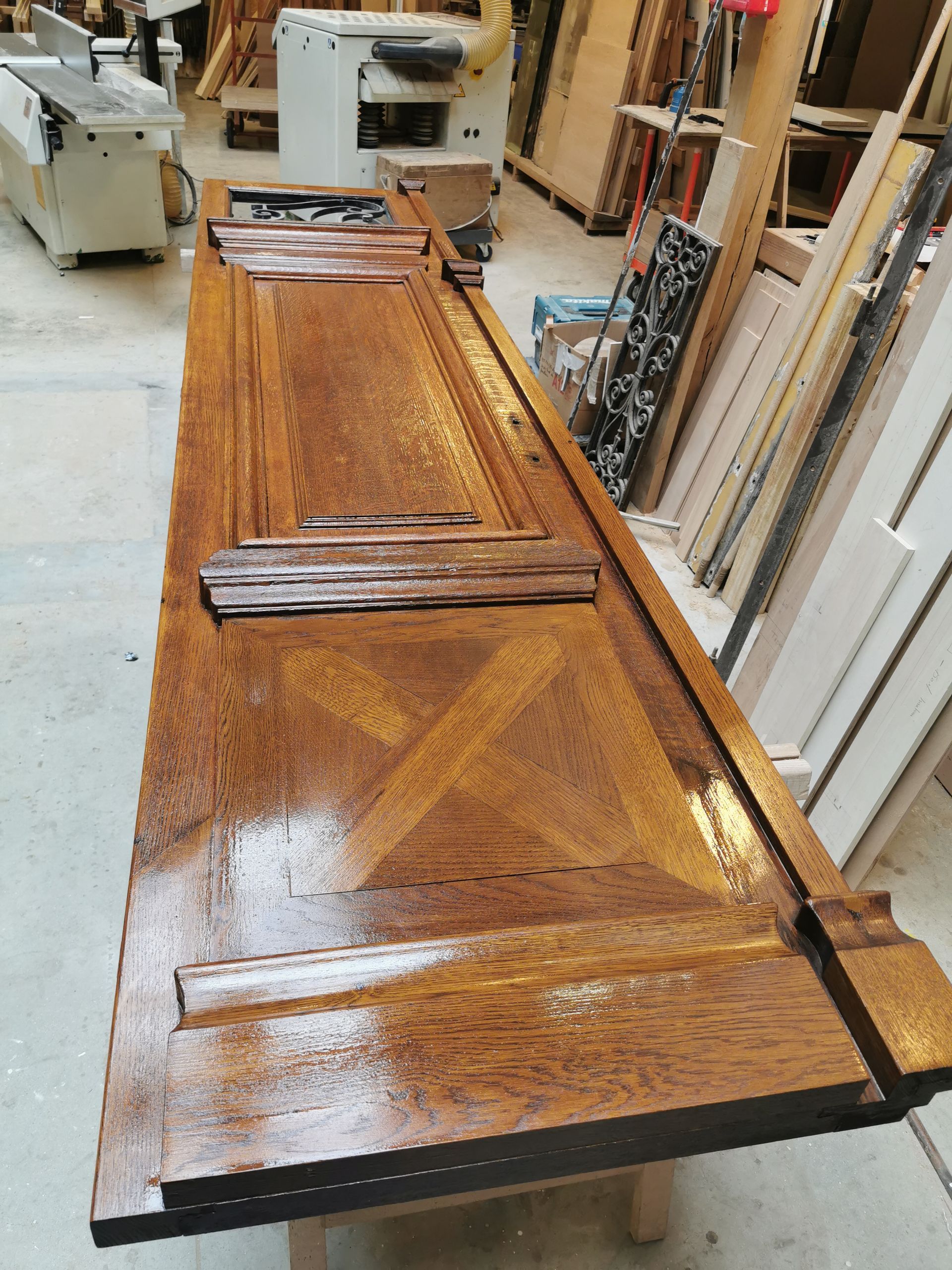 Un panneau de bois poli orné d'une incrustation en forme de X repose sur un établi dans un atelier de menuiserie.