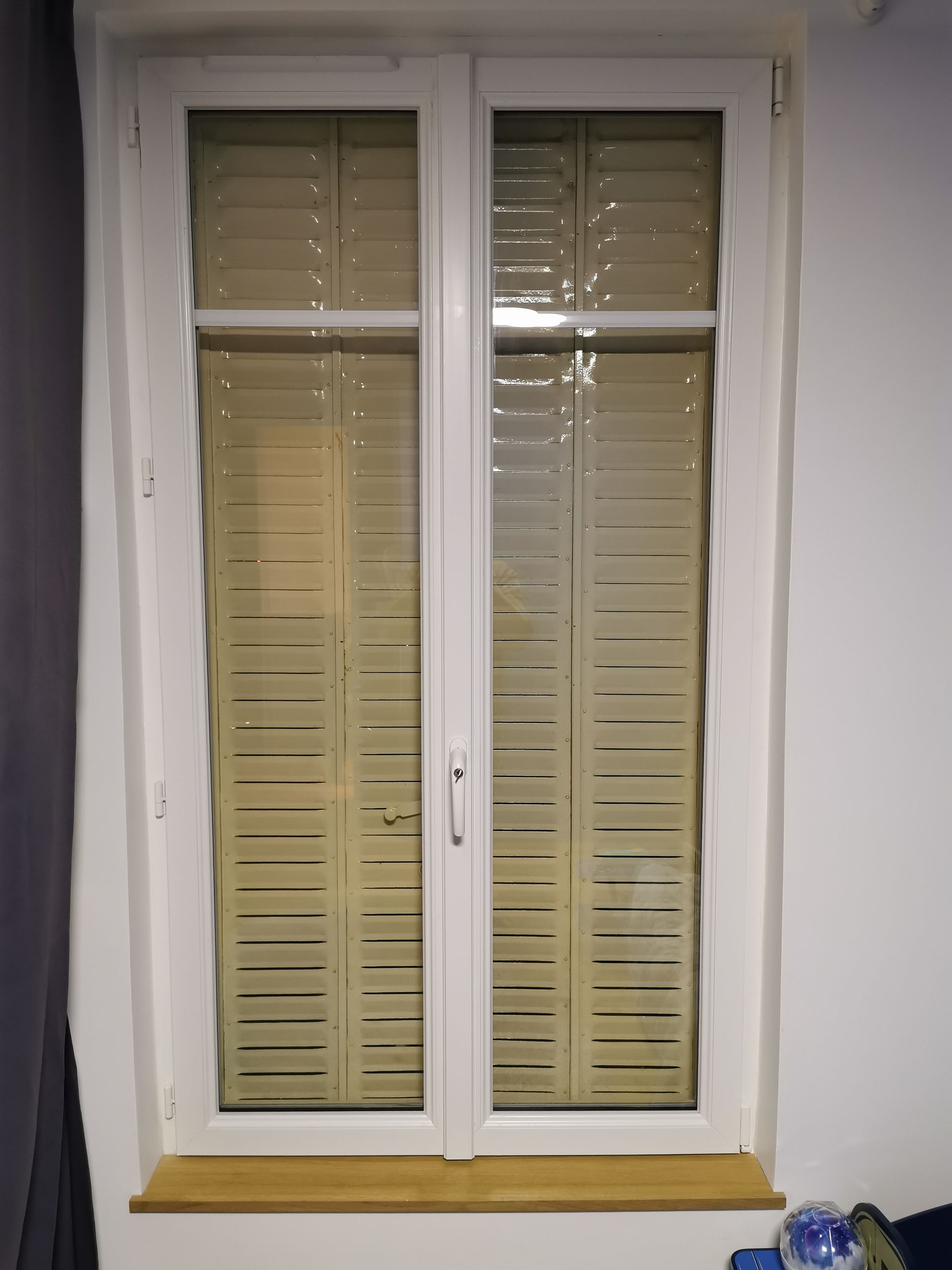 Fenêtre à double vitrage blanche avec film d'intimité translucide à rayures horizontales, encastrée dans un mur blanc avec un appui de fenêtre en bois.