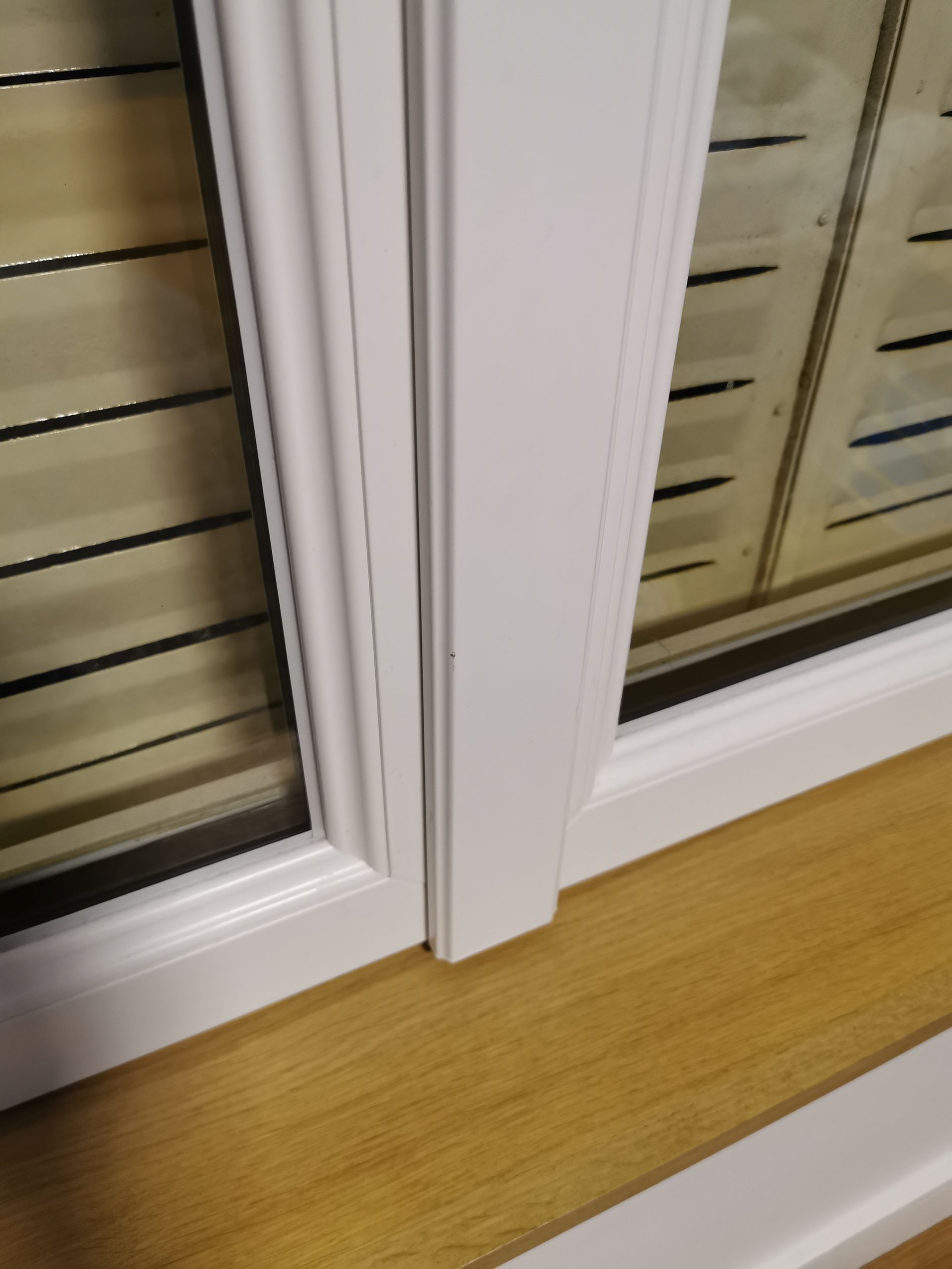 Gros plan sur un cadre de fenêtre blanc avec un montant central vertical reposant sur un appui de fenêtre lisse en bois clair.