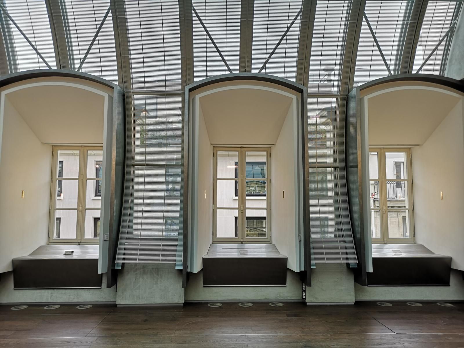 Trois fenêtres cintrées en retrait, aux cadres blancs et aux parois claires, se détachent sur une structure en verre nervurée moderne.