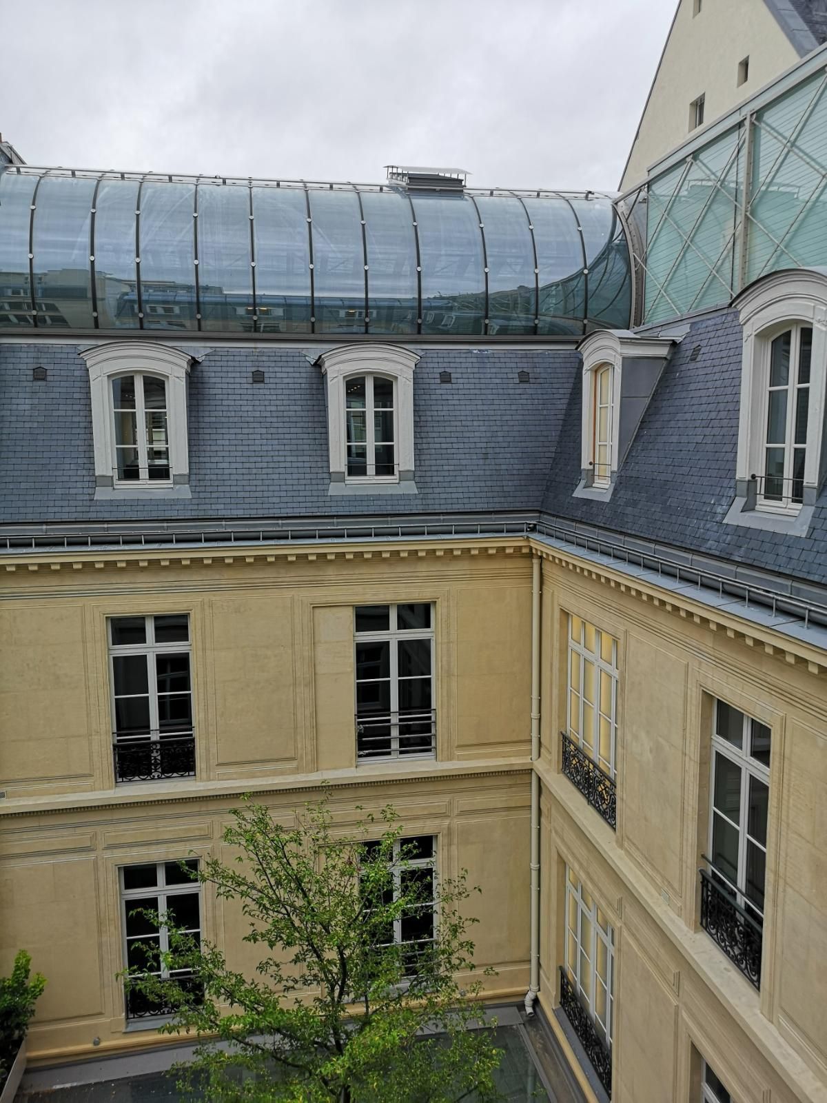 Cour intérieure du bâtiment aux murs clairs et au toit en pente bleu-gris ; toit en dôme de verre visible.