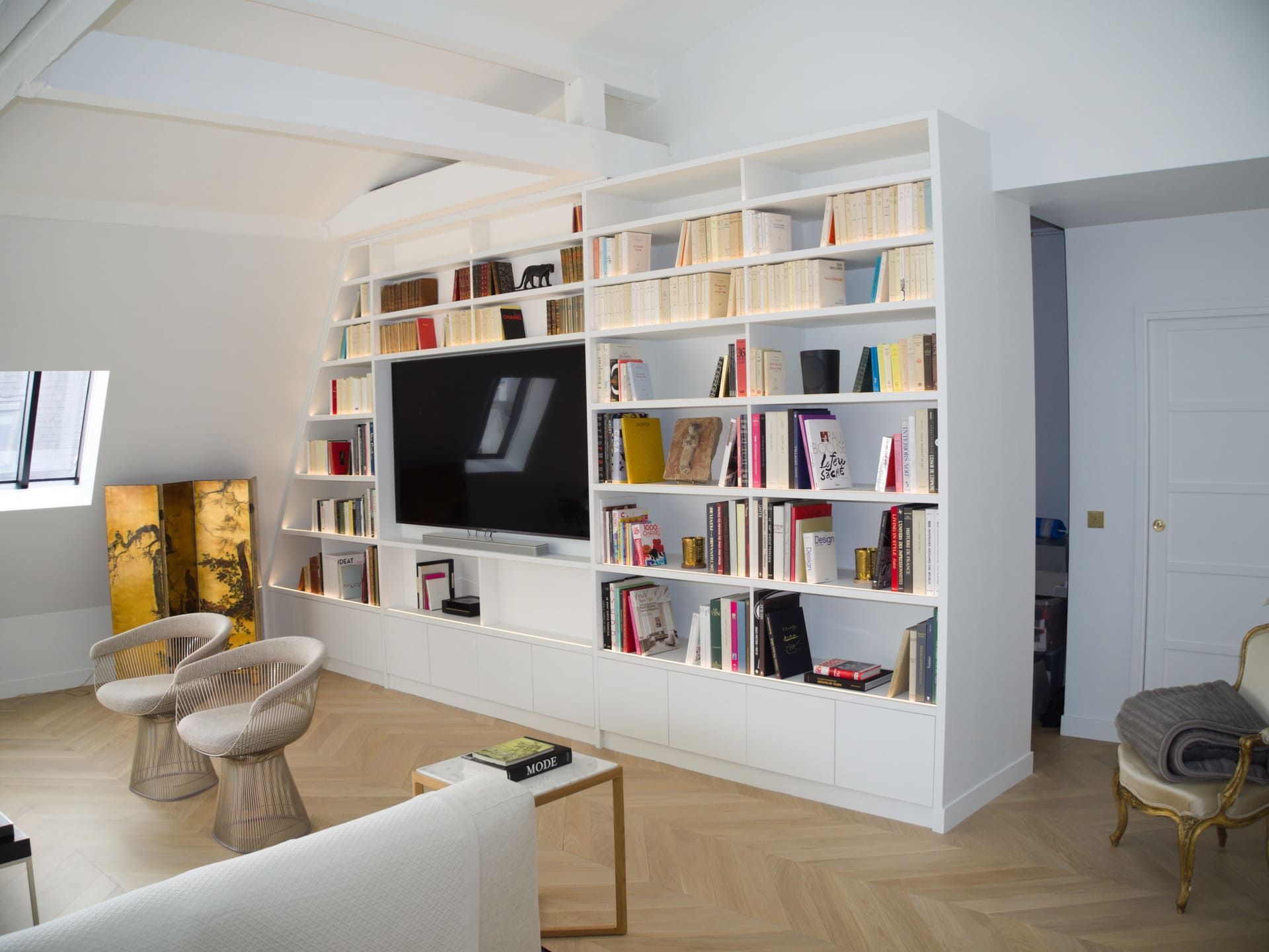 Un salon lumineux aux murs blancs, une grande bibliothèque intégrée abritant une télévision et des sièges modernes et élégants.