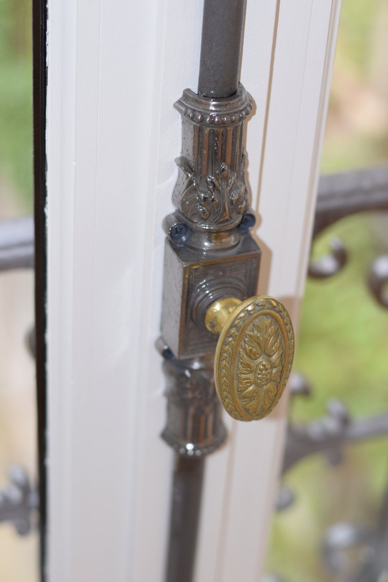 Un mécanisme de verrouillage de fenêtre vertical de style ancien avec une poignée ovale en laiton sur un cadre en bois blanc.