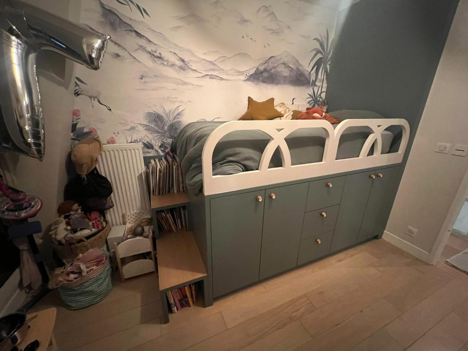 Un lit d'enfant avec rangements, escalier intégré et une fresque murale représentant une montagne.