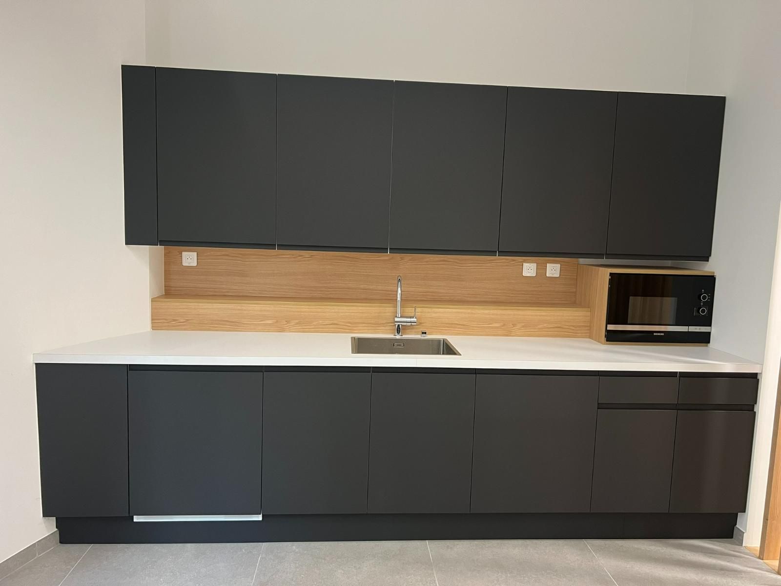 Cuisine équipée d'armoires gris foncé, d'un comptoir blanc, d'une crédence en bois et d'un micro-ondes.