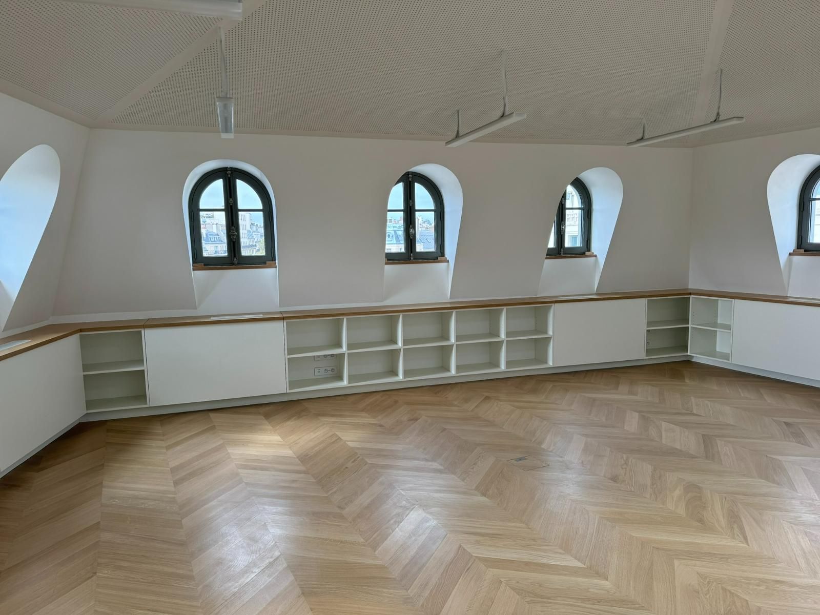 Une pièce vide avec des fenêtres cintrées, des étagères intégrées et un parquet en chevrons.