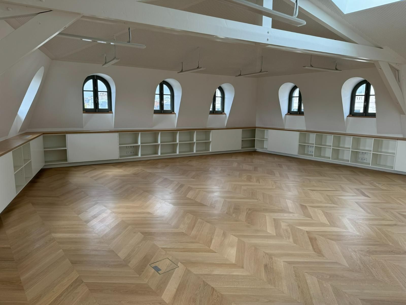 Pièce avec parquet, fenêtres cintrées, étagères intégrées et haut plafond blanc.