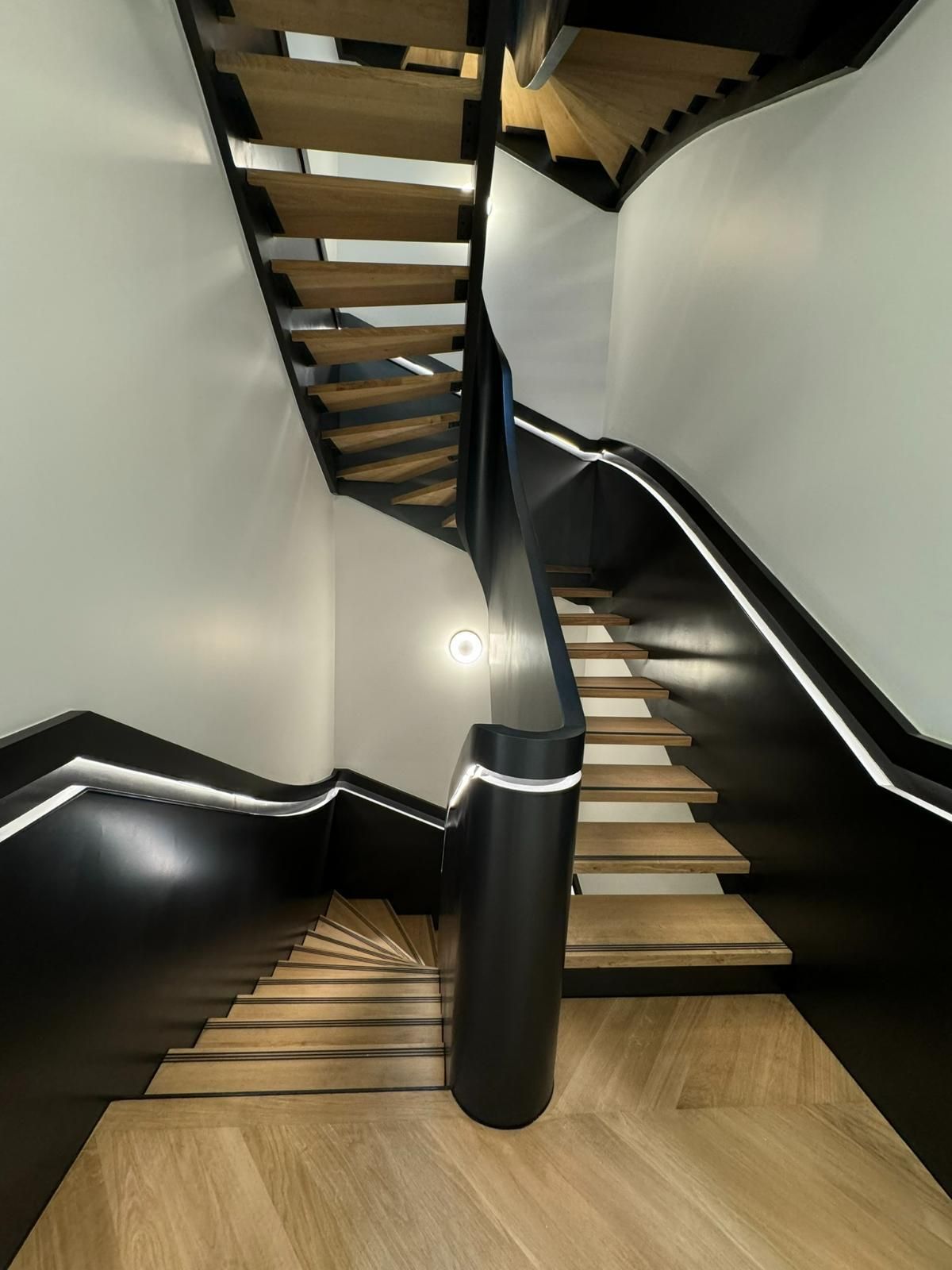 Escalier courbe avec marches en bois, rampe noire et murs avec éclairage intégré.