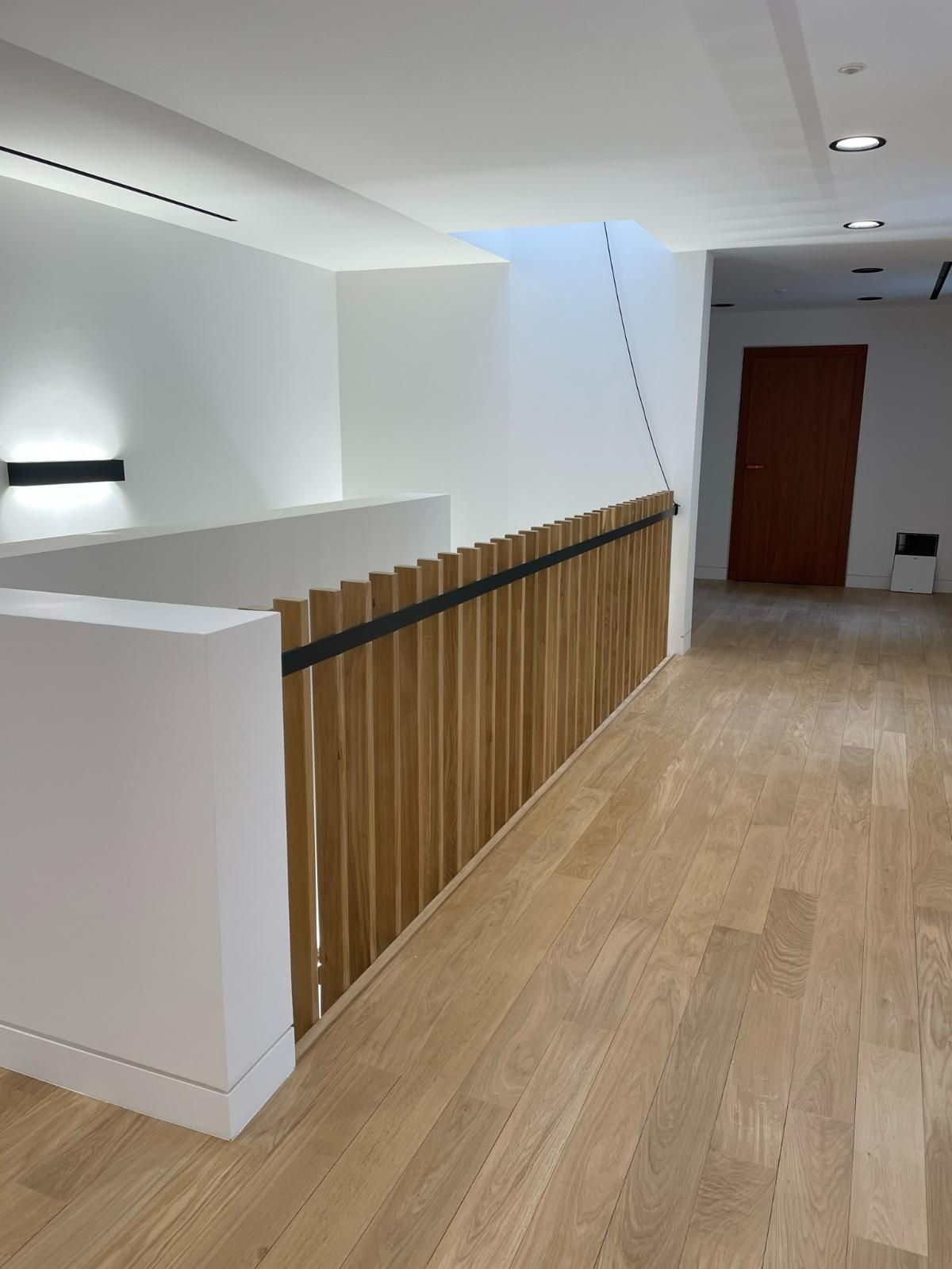 Intérieur avec balustrade en bois, murs blancs et porte rouge.