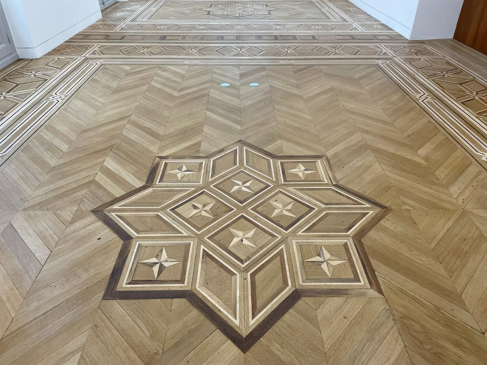 Parquet en bois à motif d'étoile à huit branches, entouré d'un motif à chevrons et de bordures décoratives.
