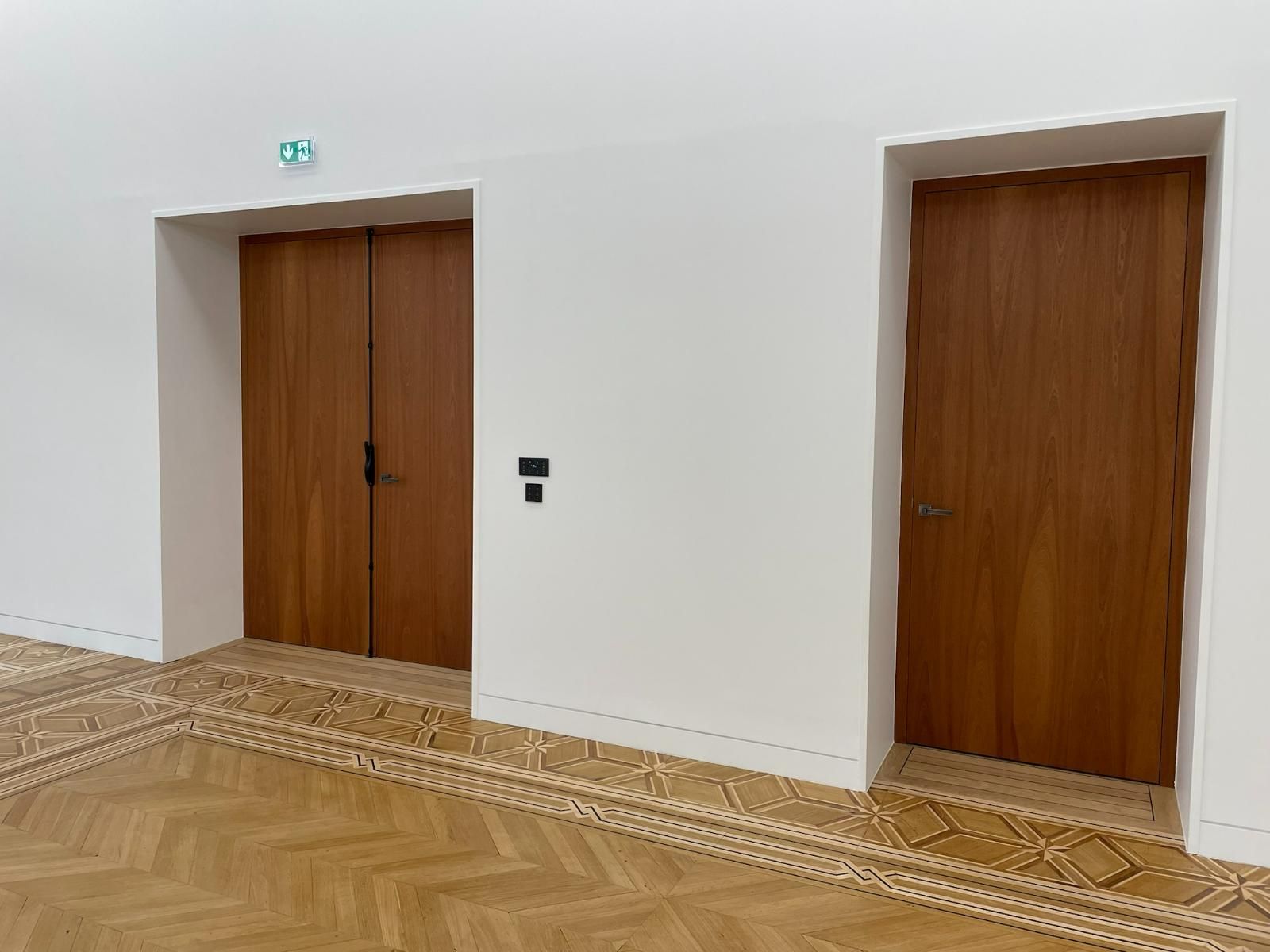 Deux portes en bois dans une pièce aux murs blancs, une double et une simple, avec un sol à motifs.