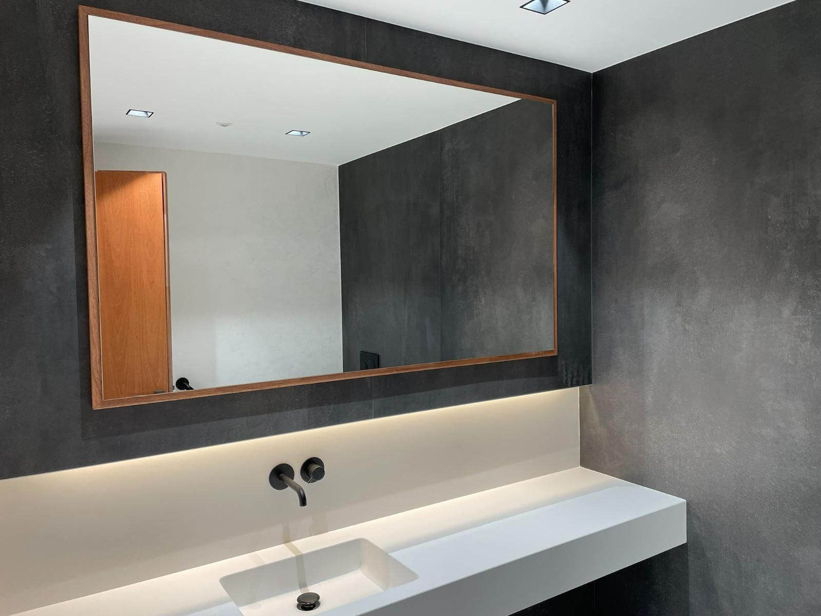 Salle de bains moderne avec grand miroir, murs gris foncé, comptoir blanc et cadre en cuivre.