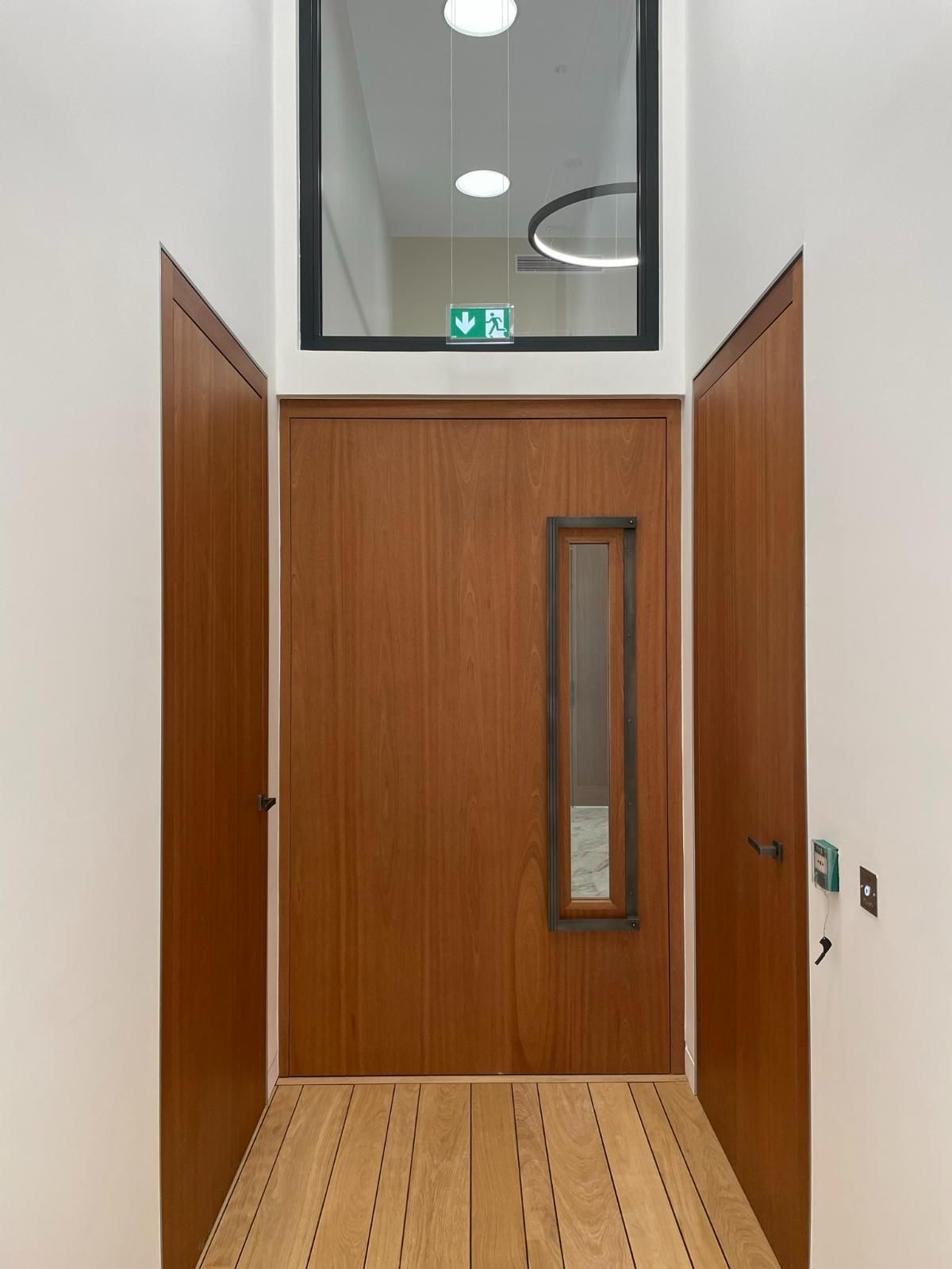 Porte en bois avec imposte, fenêtre au-dessus et panneau de sortie de secours.