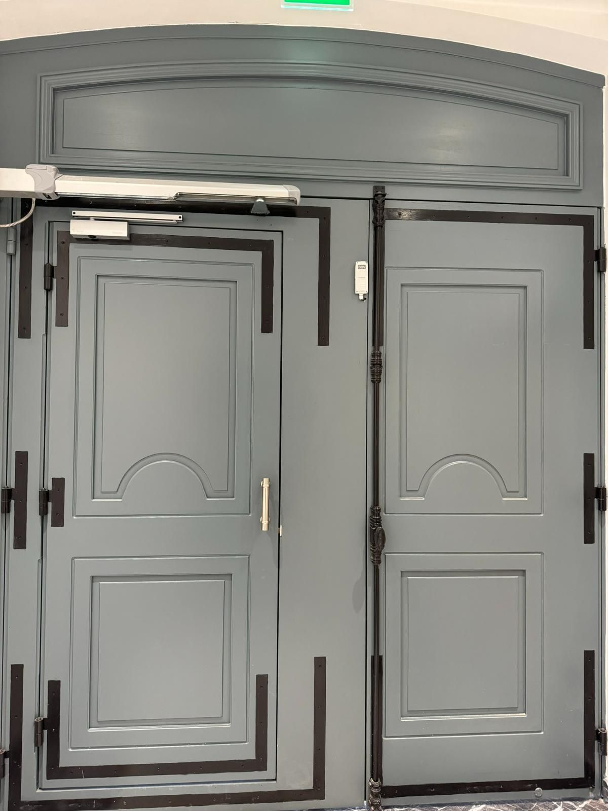 Double porte grise avec garniture noire, ouvre-porte automatique et panneau supérieur.