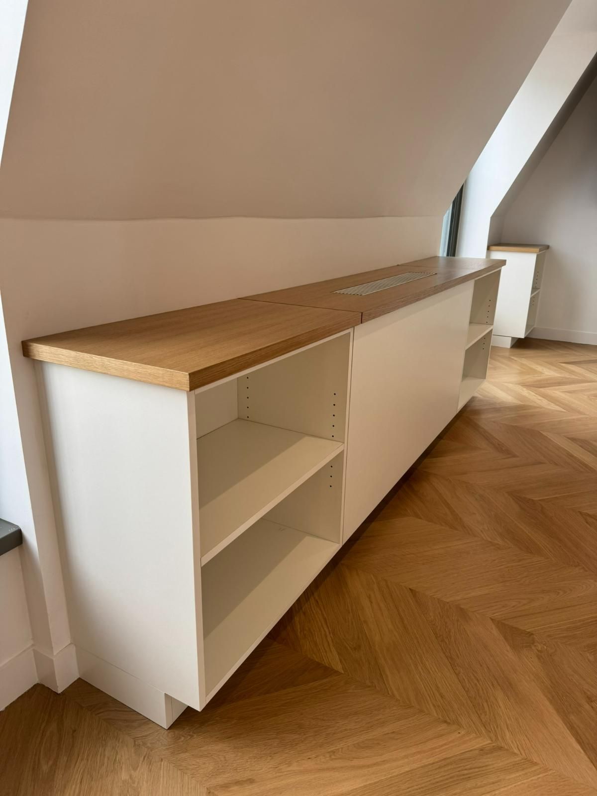 Meuble blanc avec comptoir et étagères en bois dans une pièce avec parquet.