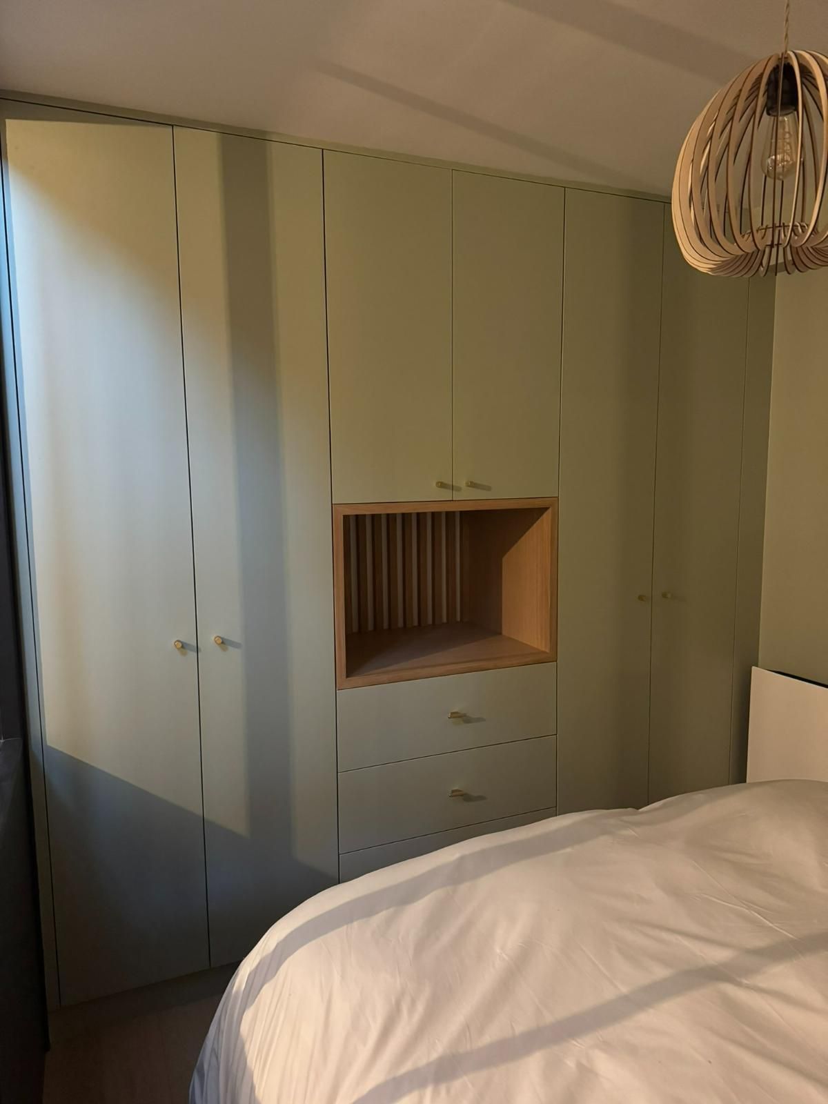 Meubles encastrés vert clair avec une niche centrale ouverte et des tiroirs, à côté d'un lit, dans une chambre.