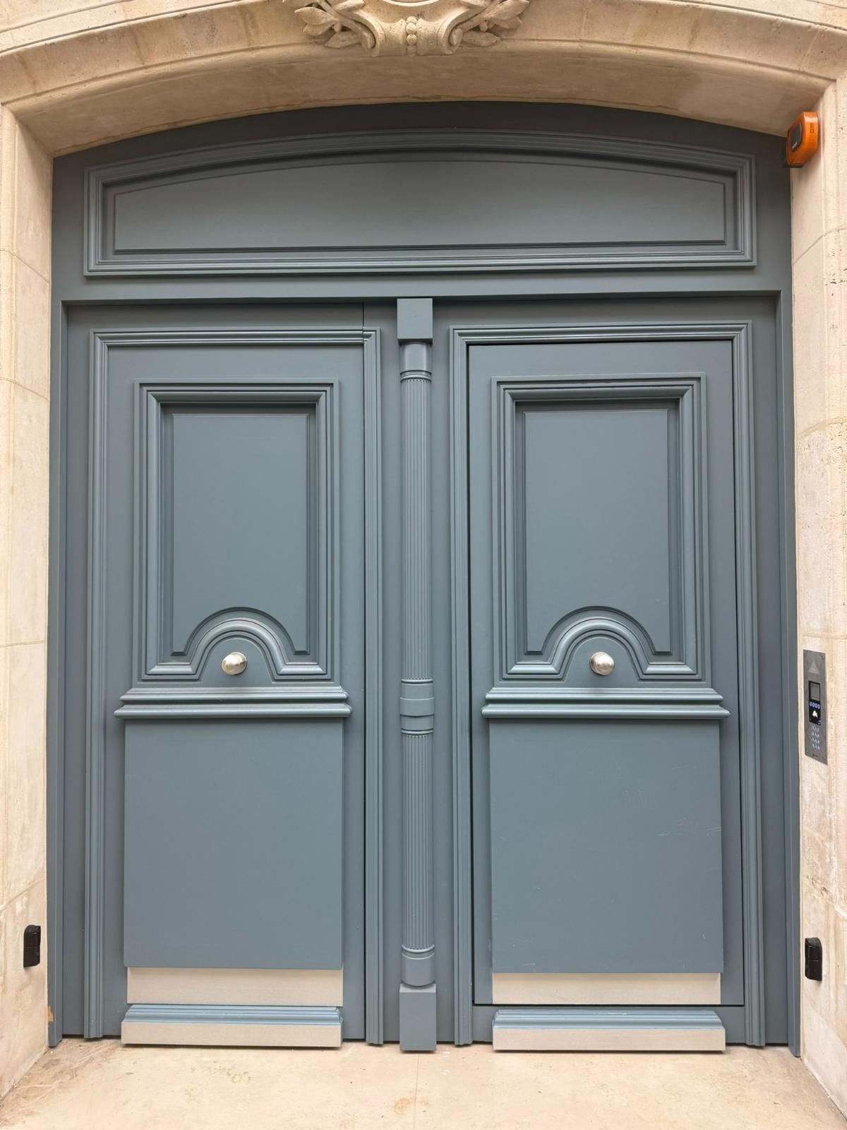 Double porte bleue avec panneaux décoratifs et arche en pierre.