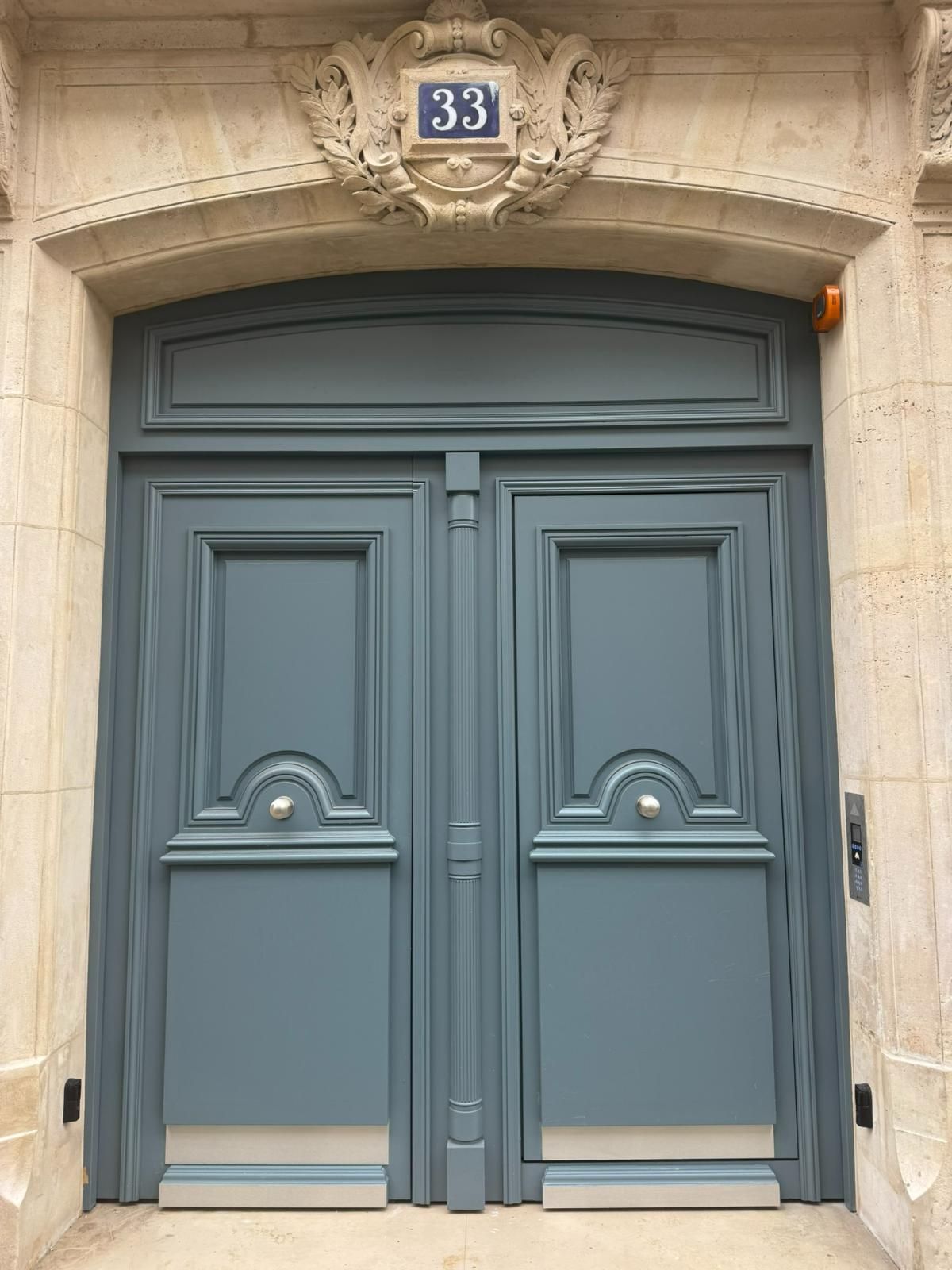 Une grande porte à double vantail bleu ardoise au numéro 33, placée dans une arche en pierre ornée de couleur claire.