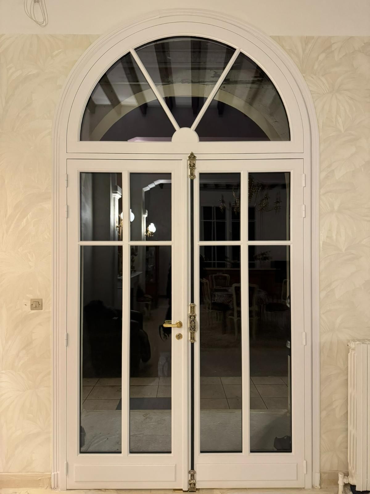 Portes doubles cintrées blanches avec panneaux de verre et quincaillerie en laiton.