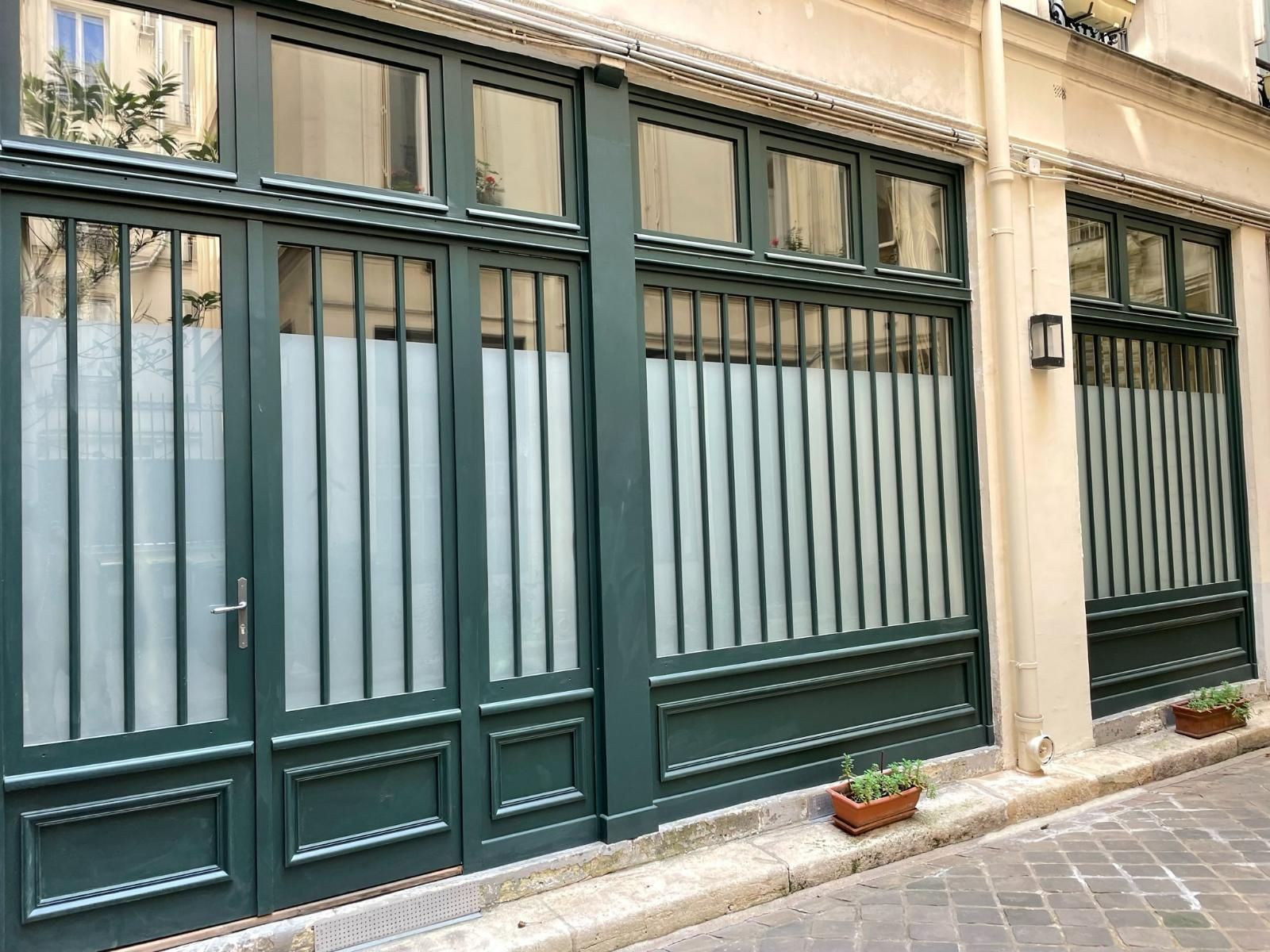 Une façade de magasin à cadre vert et vitres dépolies, encastrée dans un mur de pierre sur une rue pavée.