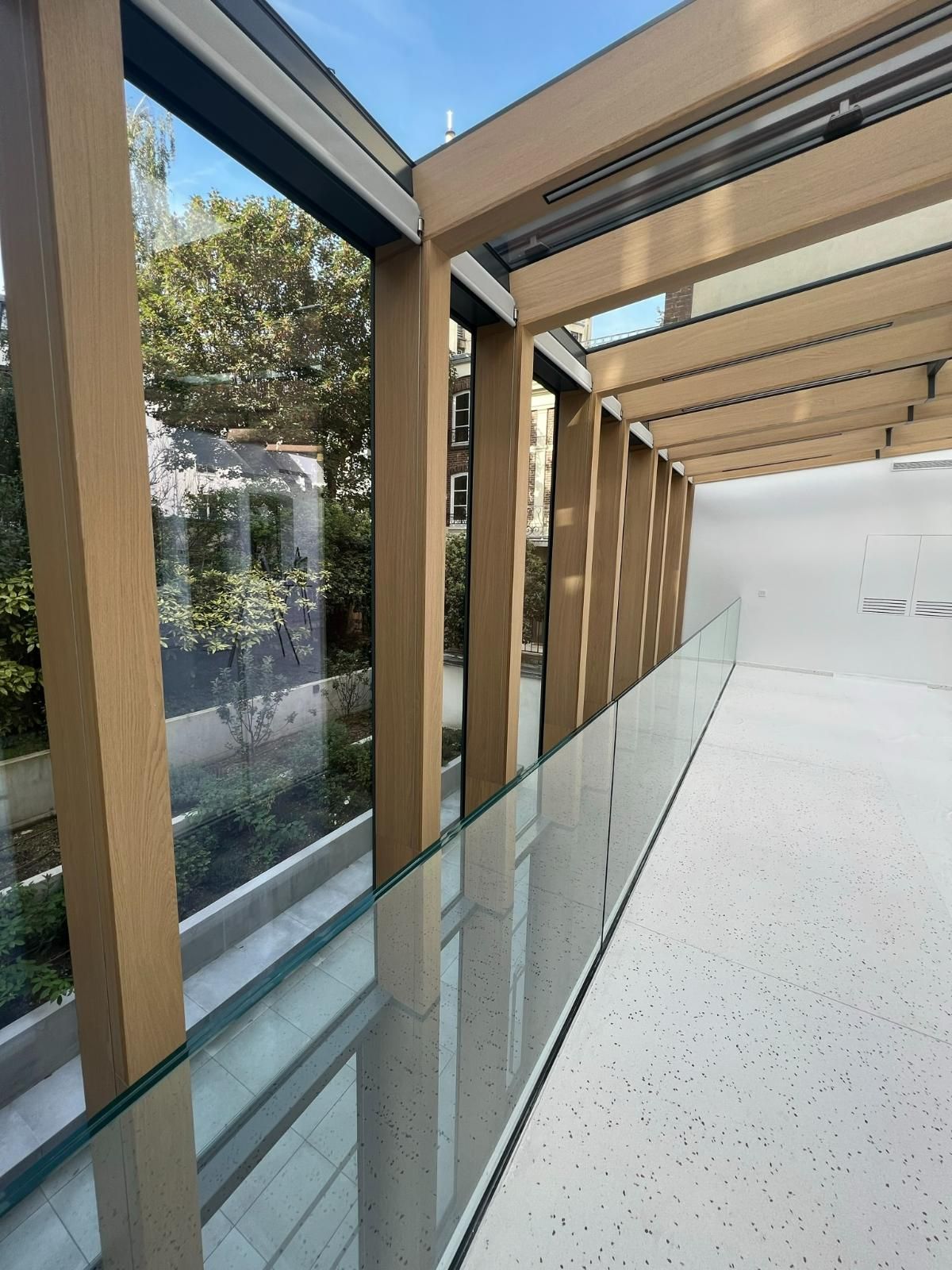 Intérieur d'un bâtiment moderne avec balustrade en verre, supports en bois et vue sur la verdure extérieure.