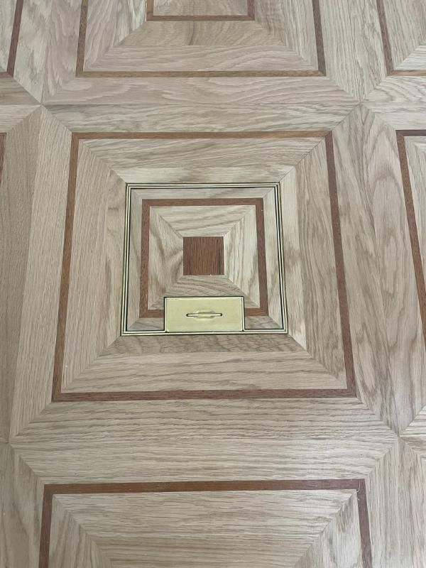 Une plaque de prise de sol en laiton, centrée dans un parquet en bois clair et foncé à motifs carrés.