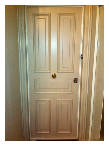 Une porte à panneaux couleur crème dans un cadre de porte avec une poignée de porte centrale dorée et une serrure argentée sur le côté.