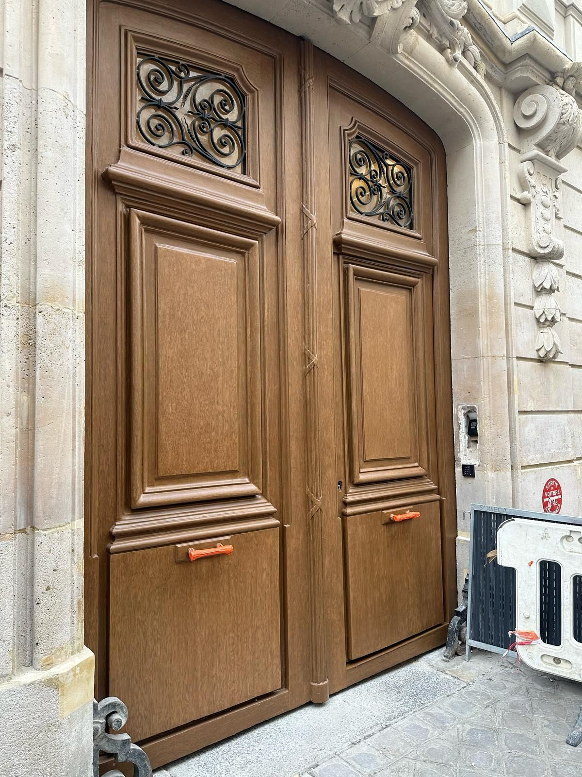 Double porte en bois avec ferronnerie et poignées orange, encastrée dans une façade en pierre.
