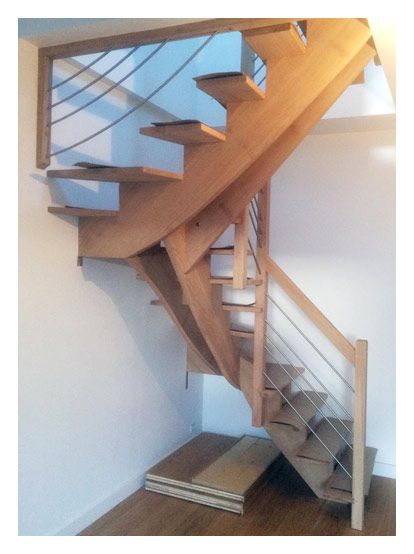 Un escalier en bois en forme de U avec des contremarches ouvertes, une finition claire et un système de garde-corps en câbles métalliques fins.