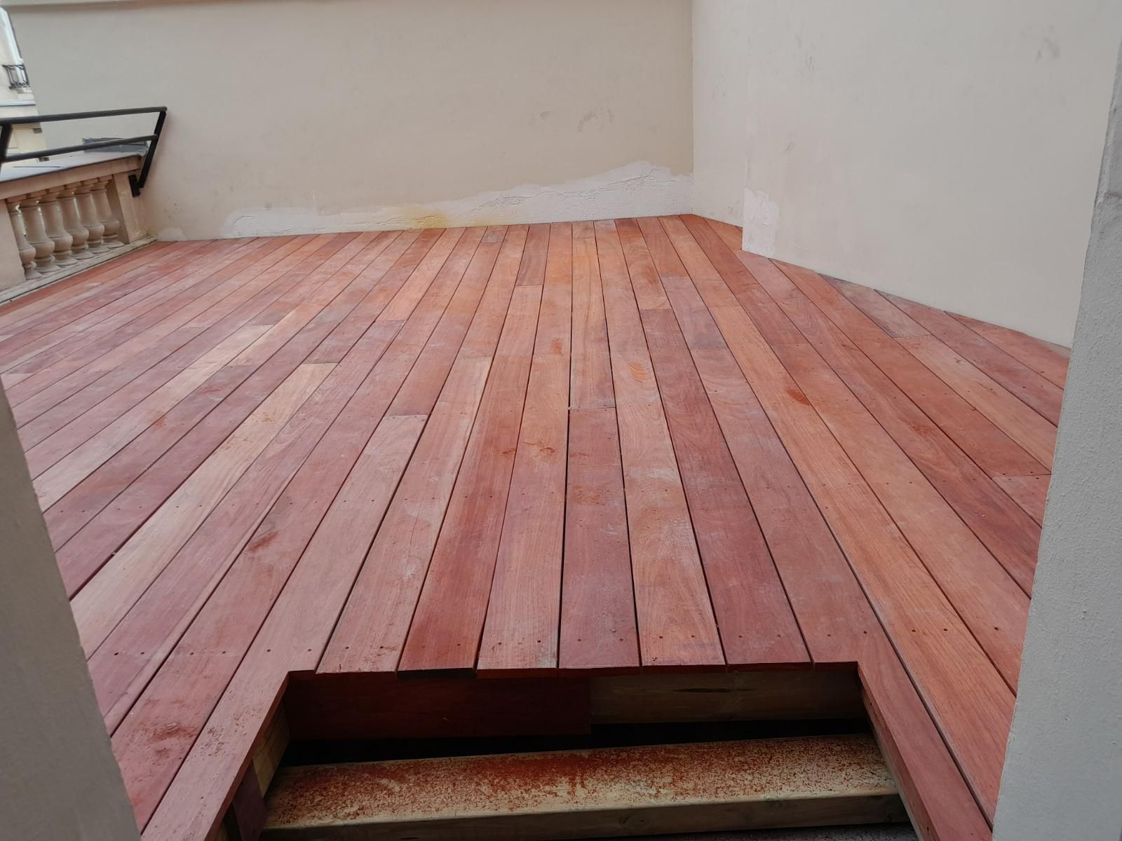 Terrasse en bois installée, entourée de murs clairs. Une ouverture est prévue en bas.