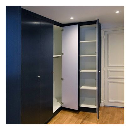 Une armoire d'angle avec des portes bleu foncé, comportant une partie ouverte avec des étagères blanches et une tringle à vêtements.