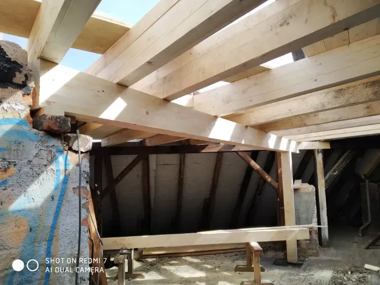 Zimmerei Andreas Karl GmbH - Dachbalken aus hellem Holz werden von Sonnenstrahlen beleuchtet