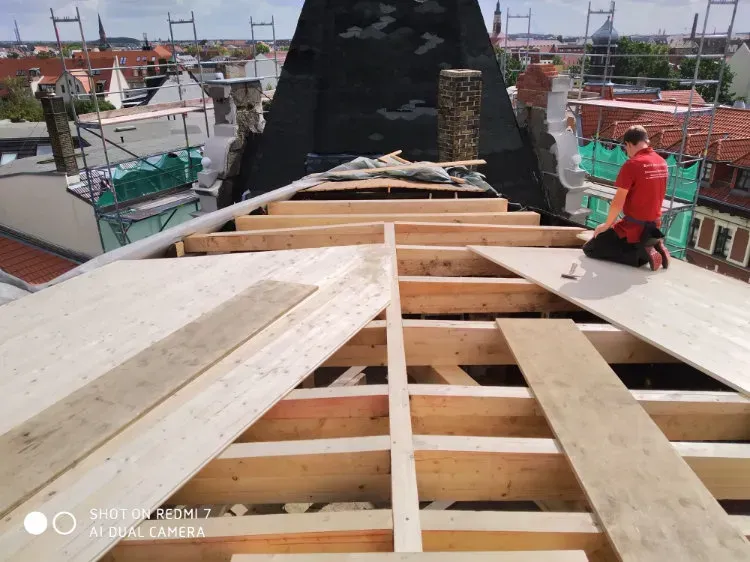 Zimmerei Andreas Karl GmbH - Person kniet auf Holzplatten, liegend auf Holzbalken eines Daches