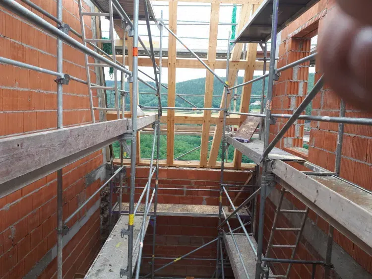 Zimmerei Andreas Karl GmbH - Baugerüste in einem Rohbau, Holzbalken, grüne Landschaft im Hintergrund