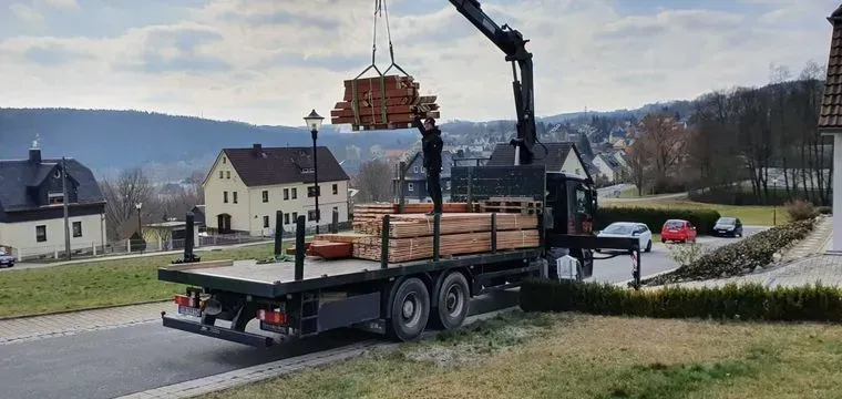 Zimmerei Andreas Karl GmbH - Transport-LKW mit Baukran entlädt Baumaterial an einer Baustelle