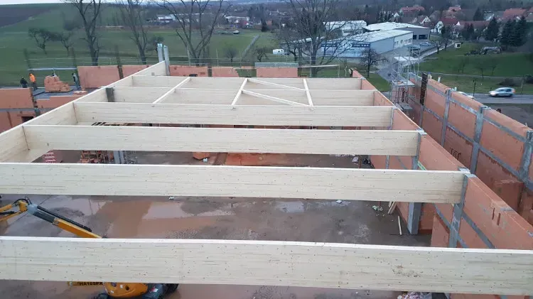 Zimmerei Andreas Karl GmbH - Blick von oben auf große Querbalken aus Holz über einem Rohbau