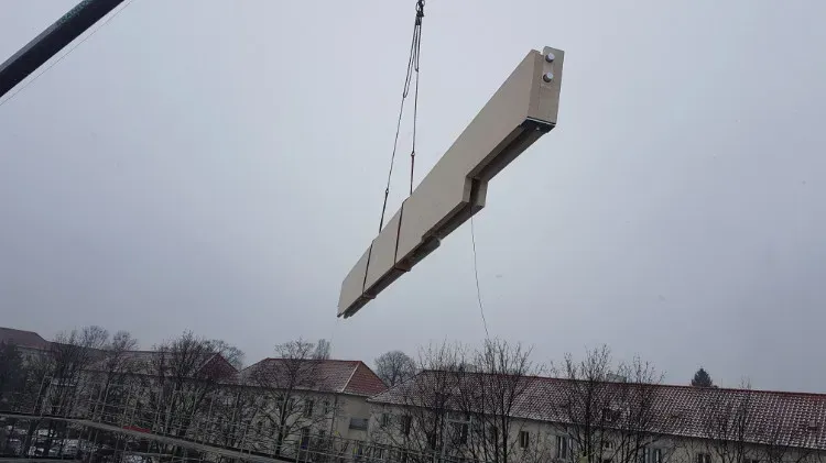 Zimmerei Andreas Karl GmbH - langes Bauteil aus Holz für Dachkonstruktion hängt am Seil eines Krans, grauer Himmel