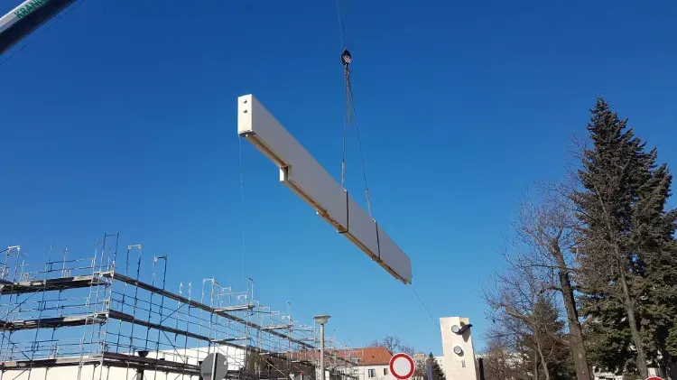 Zimmerei Andreas Karl GmbH - Baumaterial aus Holz hängt an einem Kran vor einem blauen Himmel über Baustelle