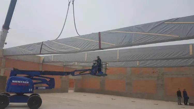 Zimmerei Andreas Karl GmbH - In graue Folie gehüllte Holzbalken im Rohbau eines Gebäudes, Mann mit Personenkran darunter