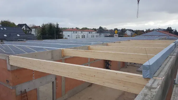 Zimmerei Andreas Karl GmbH - Holzbalken ragen zwischen zwei tragenden Wänden über ein Gebäude im Bau