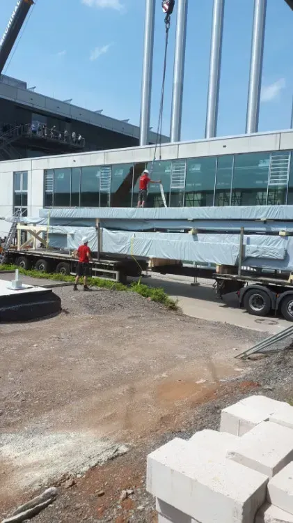 Zimmerei Andreas Karl GmbH - Arbeiter in Schutzausrüstung vor einem LKW-Anhänger mit in Folie gehüllten Bauteilen