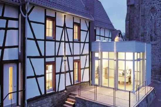 Zimmerei Andreas Karl GmbH - Saniertes Fachwerkhaus mit modernem Anbau, bei Dämmerung, hell beleuchtet